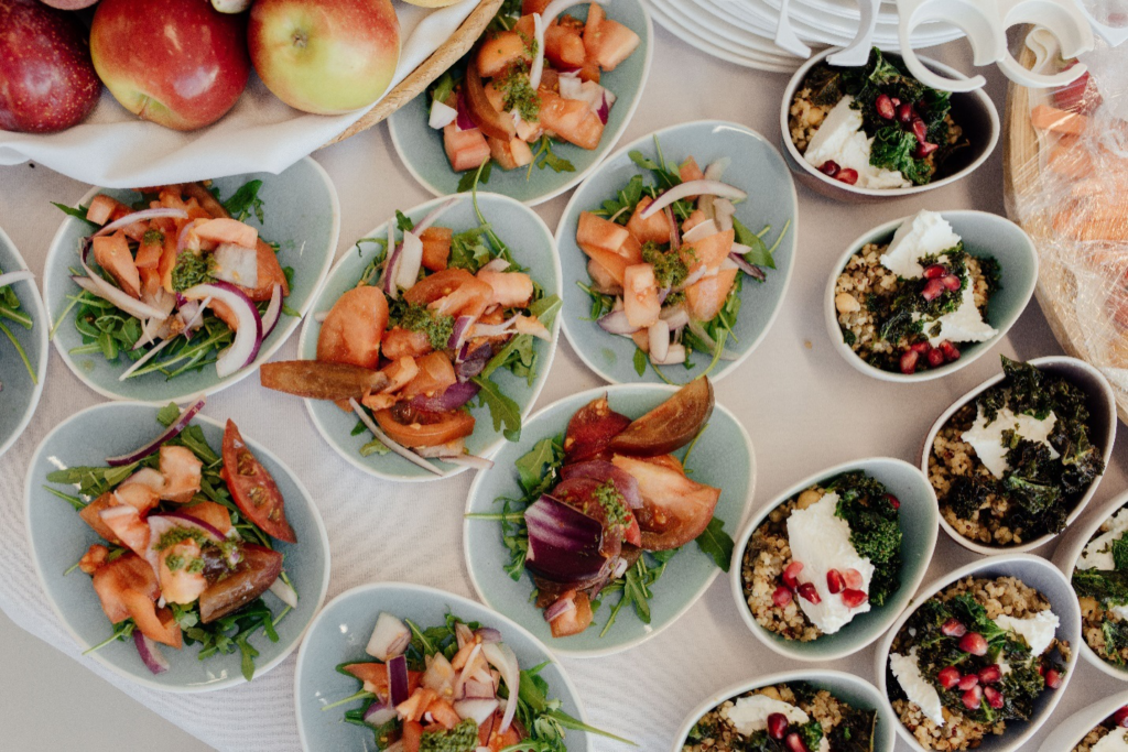 A table set up with customized salads in individual bowls next to apples showcases catering companies that incorporate trends in event catering.