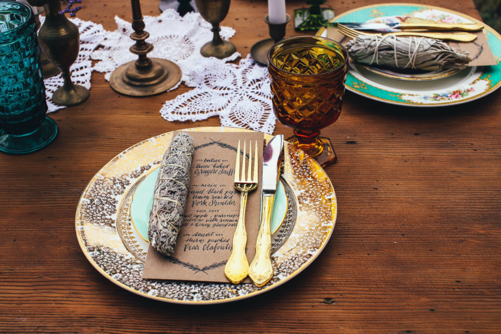 A unique printed plate with gold cutlery, a napkin, and a printed menu on top sits beside colored glassware after consulting a menu planning guide.