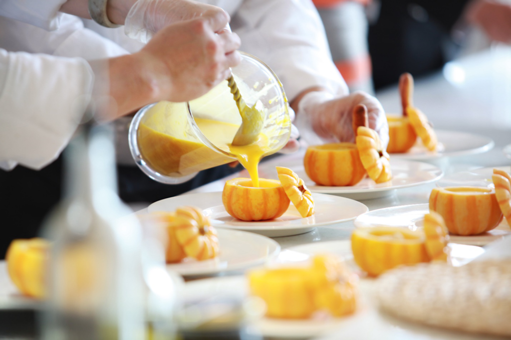 A caterer pours pumpkin soup into small pumpkins on individual plates in a personalized catering service style